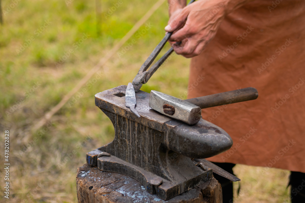 Professional blacksmith working with metal on anvil at outdoor workshop - close up view, selective focus. Handmade, reenactment, craftsmanship, medival concept