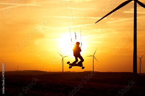 Kite land boarder jumps in front of setting sun. 1 man at an extreme sport art in action with a kiteboard. Landscape with wind turbines as silhouette. Side view. © Jan