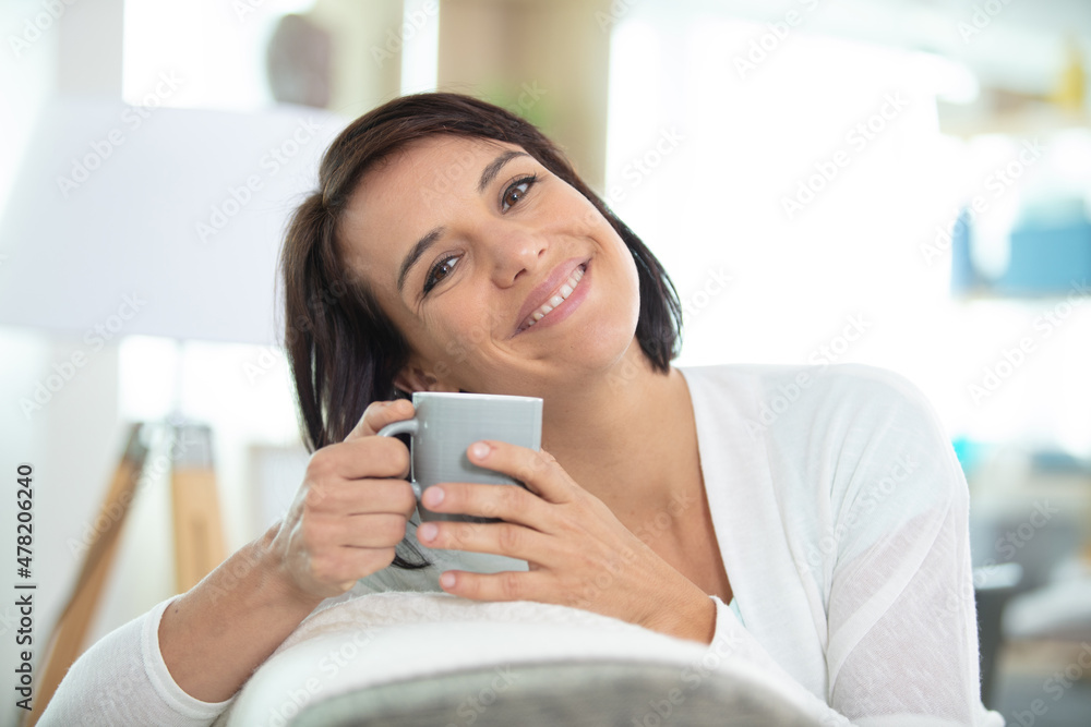 cheerful brunette drinking coffee sat on sofa