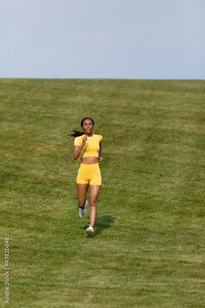 African-American woman in yellow fitness shirt and shorts runs down hill during her workout 0401