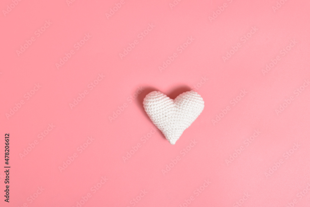 One white knitted heart lies on a pink background in the center. Background for Valentine's Day.