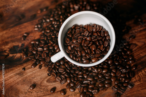 Coffee beans in a mug and scattered around the mug on a wooden table. Top view.