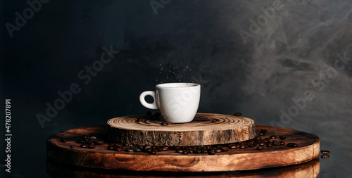 A cup of coffee with a splash of drops. Spilled coffee beans on the piece od wood. Banner on dark bacground.