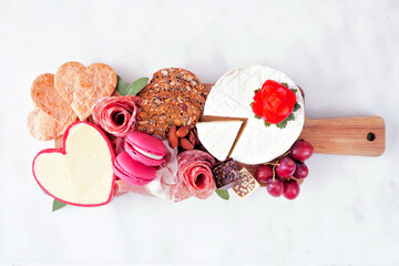 Valentine's Day charcuterie board with a selection of cheeses, appetizers and fruit. Above view on a dark wood background.