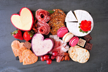 Valentine's Day charcuterie board with a variety of cheeses, appetizers and sweets. Top view on a dark slate background.
