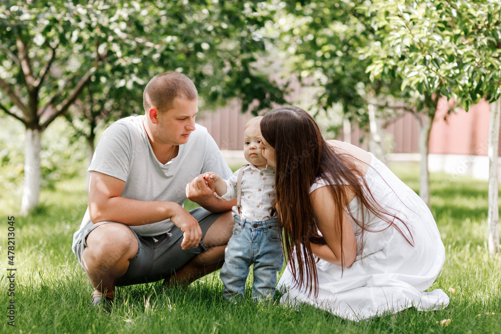 Happy young family, mom, dad and baby son spending time together outdoors in summer green garden