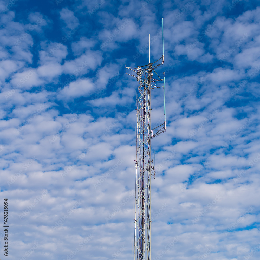 Cell tower and puffy clouds broadcasting a cellular signal to passing cars below the tower on the highway to communicate with others in the distance with no connecting wires Cell tower and puffy clouds broadcasting a cellular signal to passing cars below the tower on the highway to communicate with others in the distance with no connecting wires