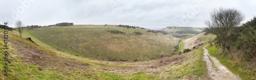 Panorama of Devil's Dyke on the South Downs of England, UK. The landscape shows the path running up the middle of the dyke, with a footpath leading into the distance and a tree in the foreground.