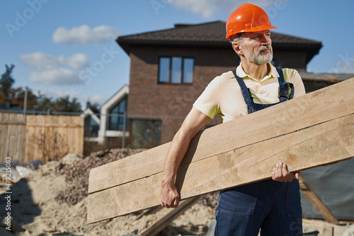 Elderly worker going through site with wooden plank