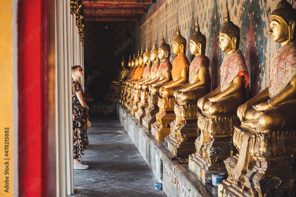 Fototapeta premium Blonde Touristin betrachtet Buddha Statuen in buddhistischem Tempel in Bagkok, Thailand
