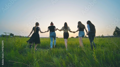 Girls friends go hand in hand at sunset across the field.