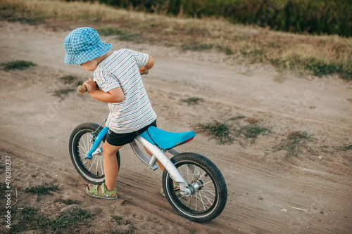 Portrait of a caucasian boy with a blue hat riding the bike on a country road in a summer day. Childreday2020 photo