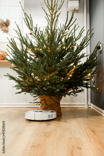 Smart home. Robot vacuum cleaner performs automatic cleaning. Cleans the parquet from Christmas tree needles after the new year. cleans near the Christmas tree after the holidays. © Andriy Medvediuk