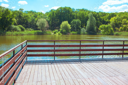 Observation deck with wooden balustrade at the lake . Pond on a summer day