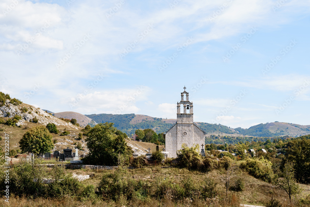 Old chapel with a bell tower near the cemetery in the field against the background of mountains