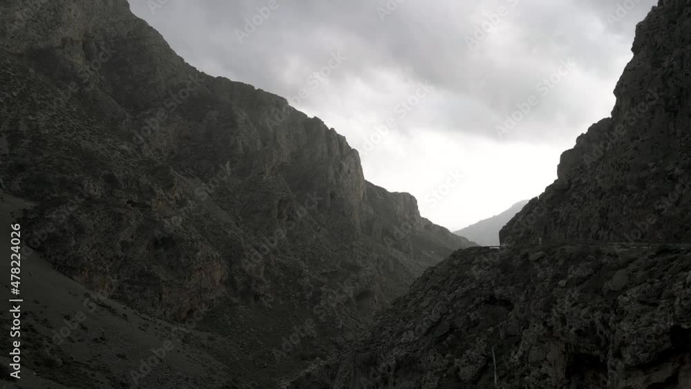 Man sitting on top of rock looking towards Samaria gorge , valley, Crete Island Greece. Aerial pullback Man sitting on top of rock looking towards Samaria gorge , valley, Crete Island Greece. Aerial pullback