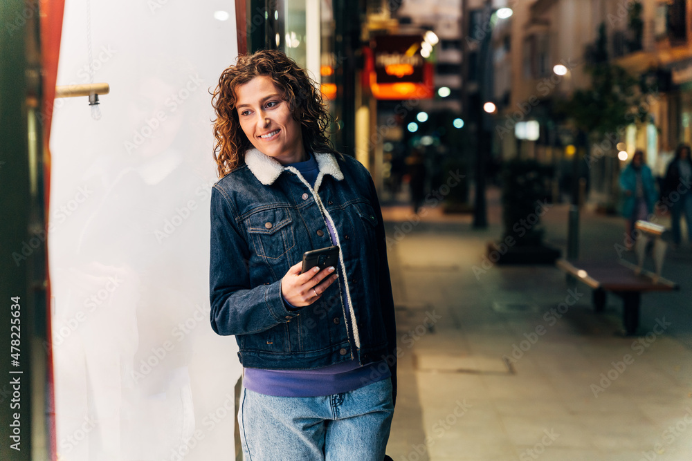 Cheerful young woman with smartphone standing on street