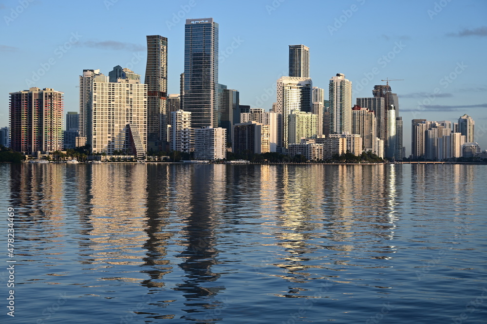 City of Miami skyline reflected on tranquil water of Bisvcayne Bay in early morning light on calm clear winter day.