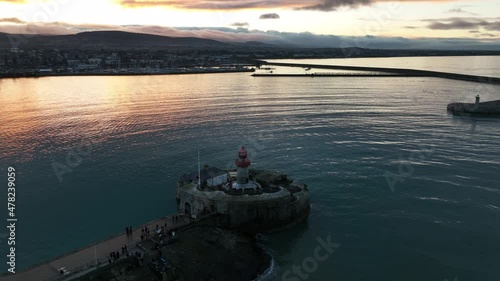 Dún Laoghaire Harbour, Dublin, Ireland. December 2021 Drone gradually pulls away from the East Pier lighthouse at a higher altitude with the Wicklow Mountains in the distance at golden-hour. photo