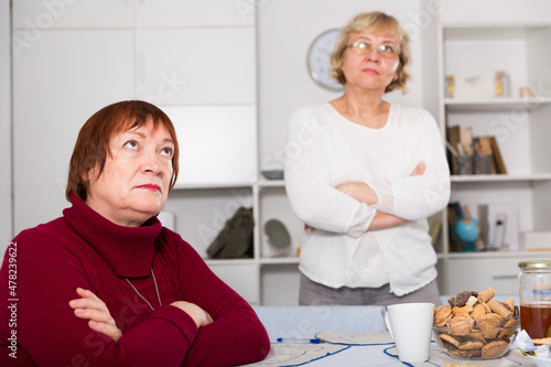 Pensioners females quarreling at kitchen near food at the table