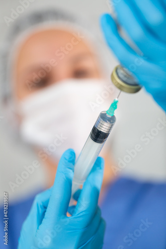 Masked female nurse working at the hospital fills a syringe with saline for injection in the treatment room. Close-up ..portrait