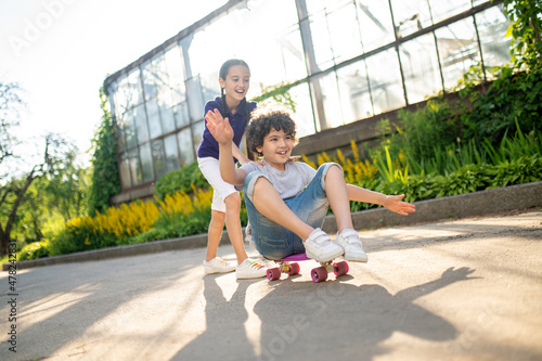 Smiling joyous young lady supporting a boy during skateboarding