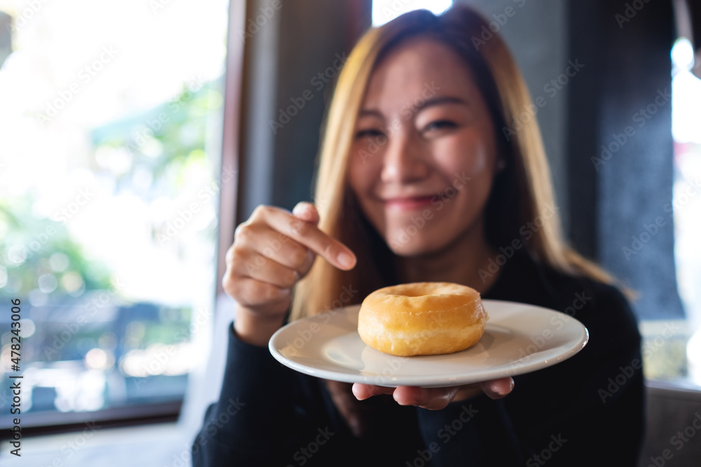 A young asian woman holding and pointing finger at a donut