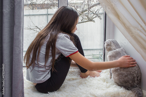 Fotografi The child is resting on the windowsill and looking out the window with a lop-eared cat