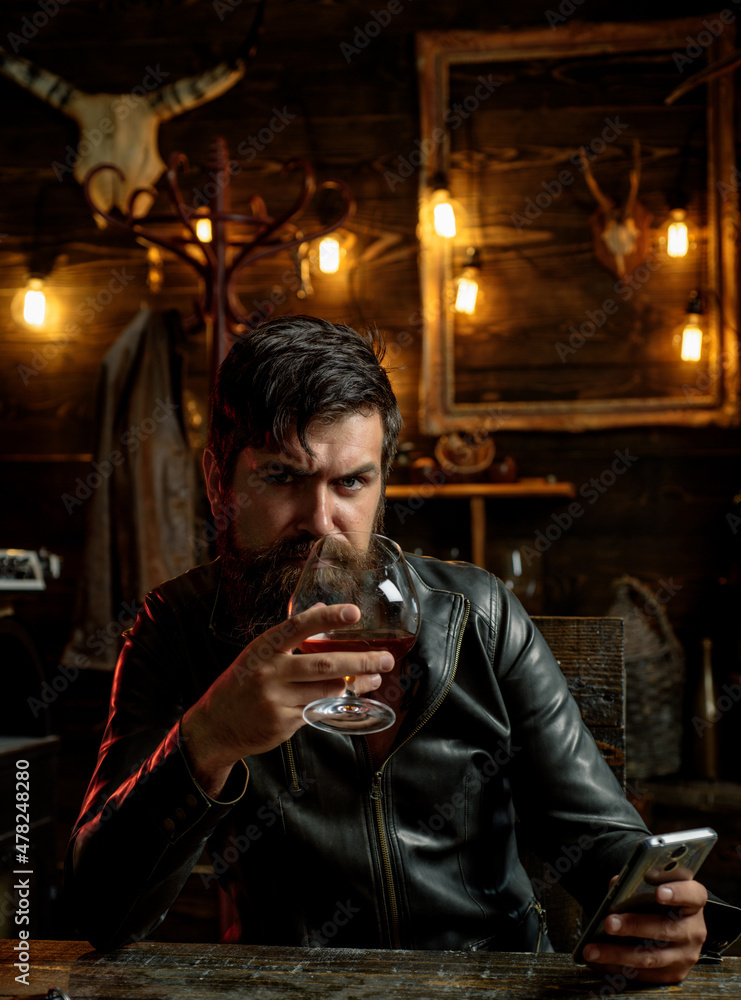 Obraz premium Stylish elegant bearded man holds whiskey glass. Social media addiction, alcohol abuse.