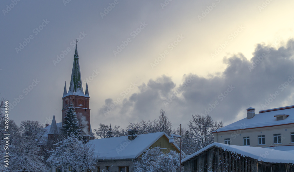 Red brick church with a green roof in winter. Cloudy skies. Sunlight between the clouds. snow covered house roofs