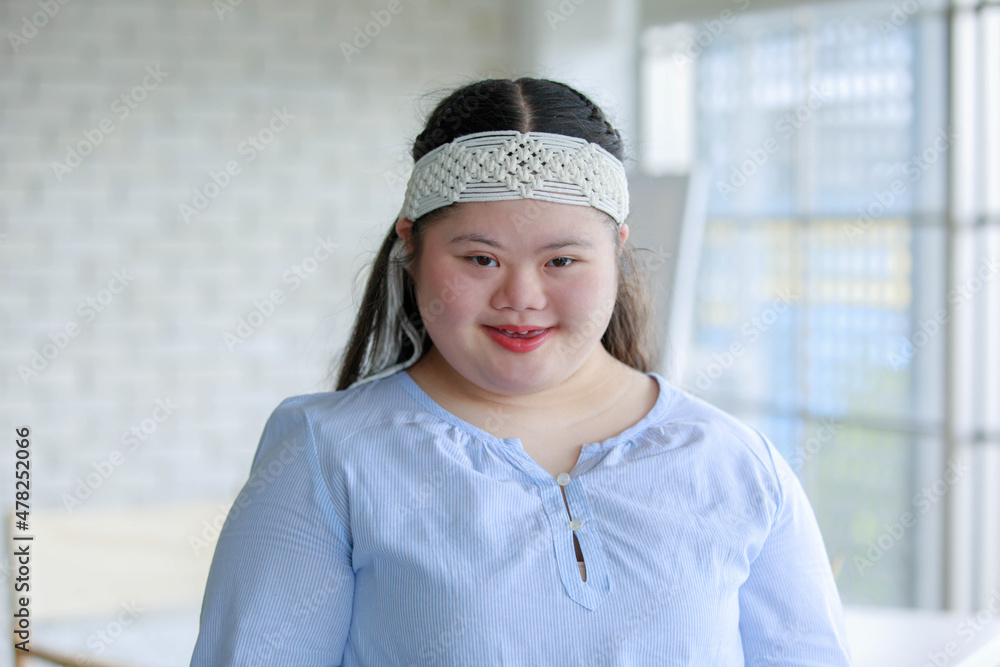 Portrait close up shot of Asian young happy chubby down syndrome autistic autism girl model wearing white knitted headband standing smiling look at camera in front blurred glass windows background Portrait close up shot of Asian young happy chubby down syndrome autistic autism girl model wearing white knitted headband standing smiling look at camera in front blurred glass windows background