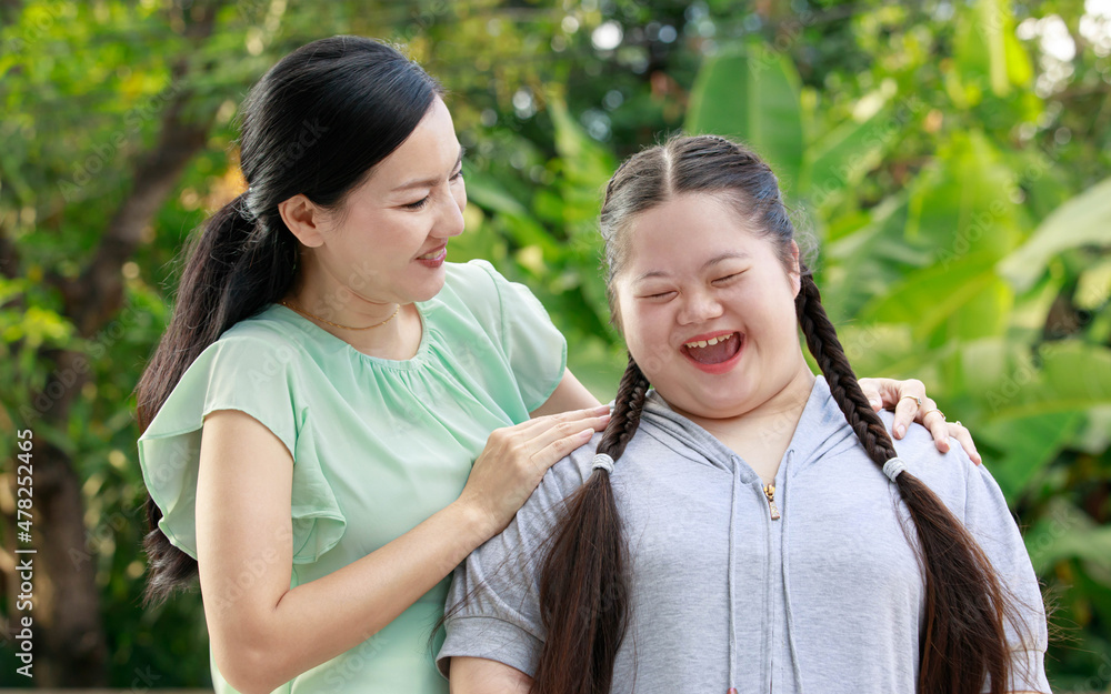 Portrait shot of Asian mother and young chubby down syndrome autistic autism little cute girl with braid pigtail hairstyle stand hugging cuddling embracing together with love smiling look at camera Portrait shot of Asian mother and young chubby down syndrome autistic autism little cute girl with braid pigtail hairstyle stand hugging cuddling embracing together with love smiling look at camera