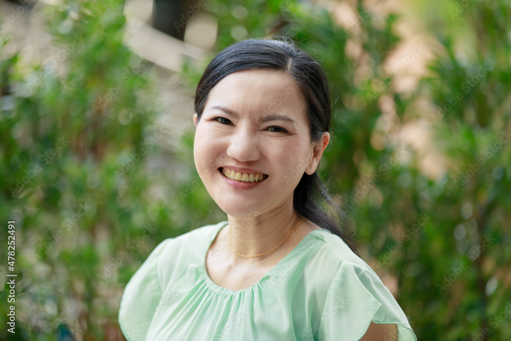 Portrait shot of Asian young mature beautiful happy pretty long ponytail hairstyle female model in green casual outfit standing posing smiling look at camera in front blurred garden view background Portrait shot of Asian young mature beautiful happy pretty long ponytail hairstyle female model in green casual outfit standing posing smiling look at camera in front blurred garden view background
