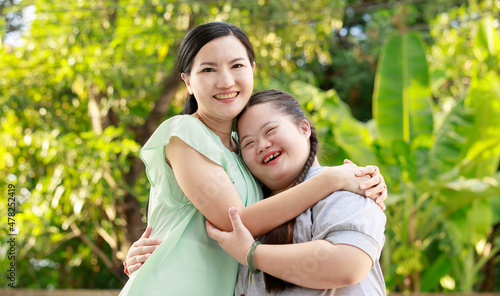 Portrait shot of Asian mother and young chubby down syndrome autistic autism little cute girl with braid pigtail hairstyle stand hugging cuddling embracing together with love smiling look at camera