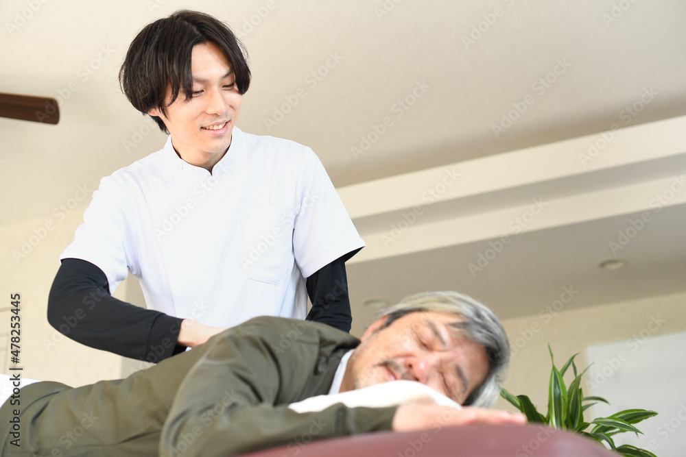 若い整体師の男性とマッサージを受けるシニア男性 若い整体師の男性とマッサージを受けるシニア男性