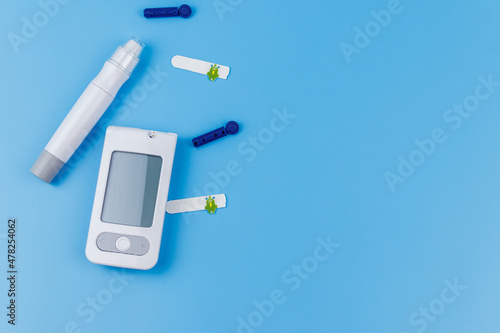 Digital glucometer, lancet pen, disposable needles and test strips on pastel blue background. Top view, copy space. Diabetes concept