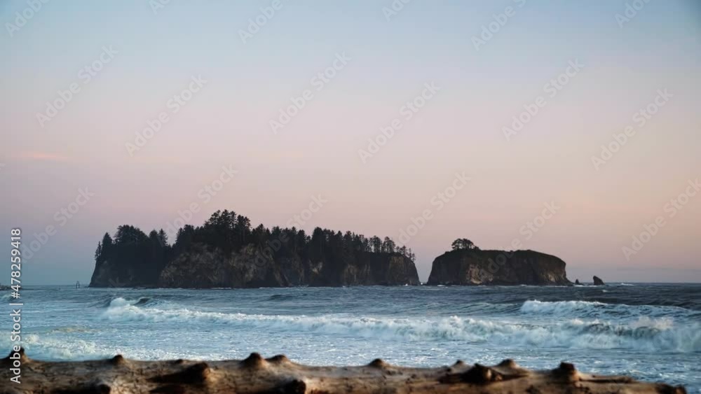 Gorgeous landscape beach shot of driftwood with waves crashing in the background, a beautiful small cliff island, and a colorful cloudy sky during sunset at the famous Ruby Beach in Forks, Washington. Gorgeous landscape beach shot of driftwood with waves crashing in the background, a beautiful small cliff island, and a colorful cloudy sky during sunset at the famous Ruby Beach in Forks, Washington.