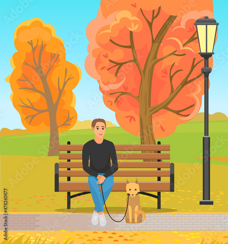 Walking with puppy in nature concept. Man with dog sits on bench with leash in his hand. Guy while walking with dog in autumn park. Person with pet spend time together during cold season outdoors