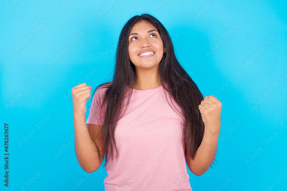 Young hispanic girl wearing pink T-shirt over blue background champion having success being glad to achieve his goals. Victory and triumph concept. Young hispanic girl wearing pink T-shirt over blue background champion having success being glad to achieve his goals. Victory and triumph concept.