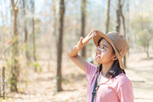 Happy beautiful young adventurous woman is smiling, using hand for covering face by hand to block, protect the sun in dry forest while walking and hiking to epic mountain. Outdoor adventure concept.