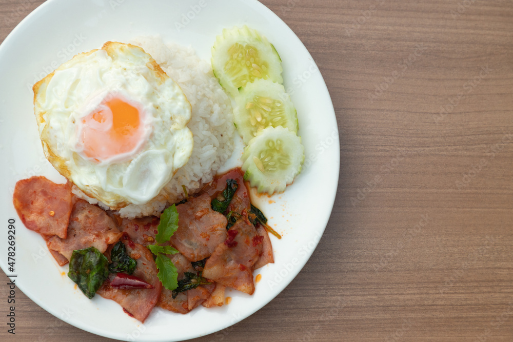 Closeup of Thai traditional fusion food, Flavorful appetizing food as Spicy bacon with basil leaves, fried egg in white modern plate on clean minimal wooden table background and texture, copy space. Closeup of Thai traditional fusion food, Flavorful appetizing food as Spicy bacon with basil leaves, fried egg in white modern plate on clean minimal wooden table background and texture, copy space.