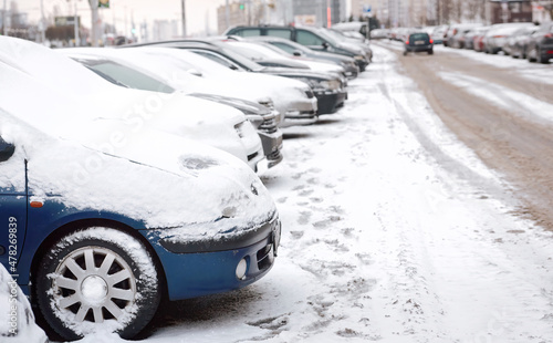 Row of parked cars covered with snow. Snow covered parking lot in the city street. Cars standing in the snowy parking lot in winter day © Tricky Shark