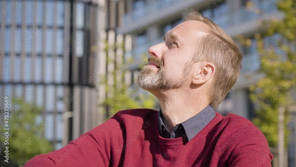 A middle-aged handsome Caucasian man looks around as he sits in a street in an urban area - office buildings in the blurry background - closeup A middle-aged handsome Caucasian man looks around as he sits in a street in an urban area - office buildings in the blurry background - closeup