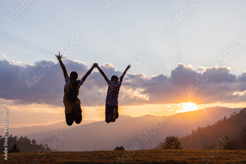 Silhouette of happy two teenage girls jumping on mountain sunset background.