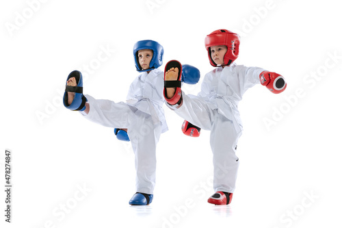 Studio shot of two little kids, boys, taekwondo athletes wearing doboks and sports uniforms isolated on white background.