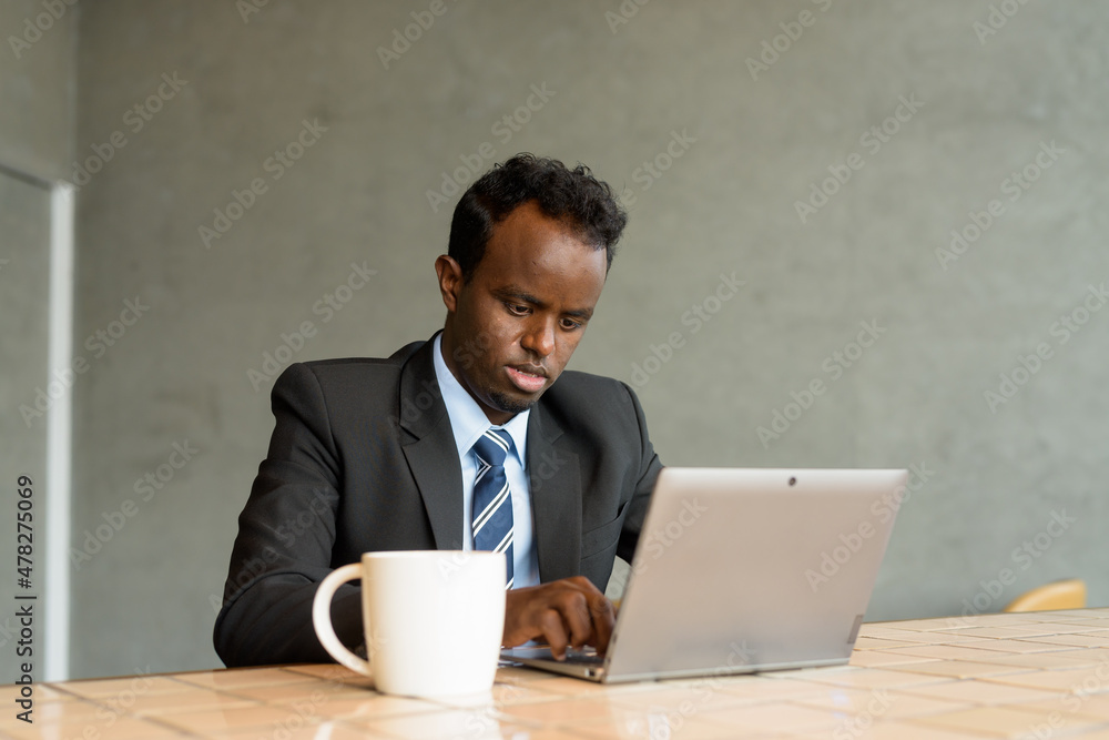African businessman wearing suit and tie in coffee shop while using laptop computer African businessman wearing suit and tie in coffee shop while using laptop computer