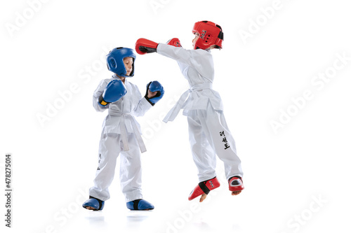 Two little kids, boys, taekwondo athletes training together isolated over white studio background. Concept of sport, education, skills