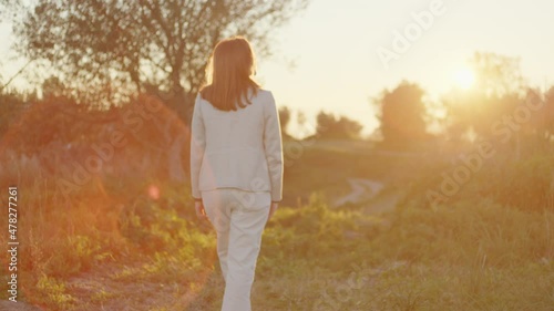 Ragazza con cappotto bianco cammina di spalle verso la natura photo