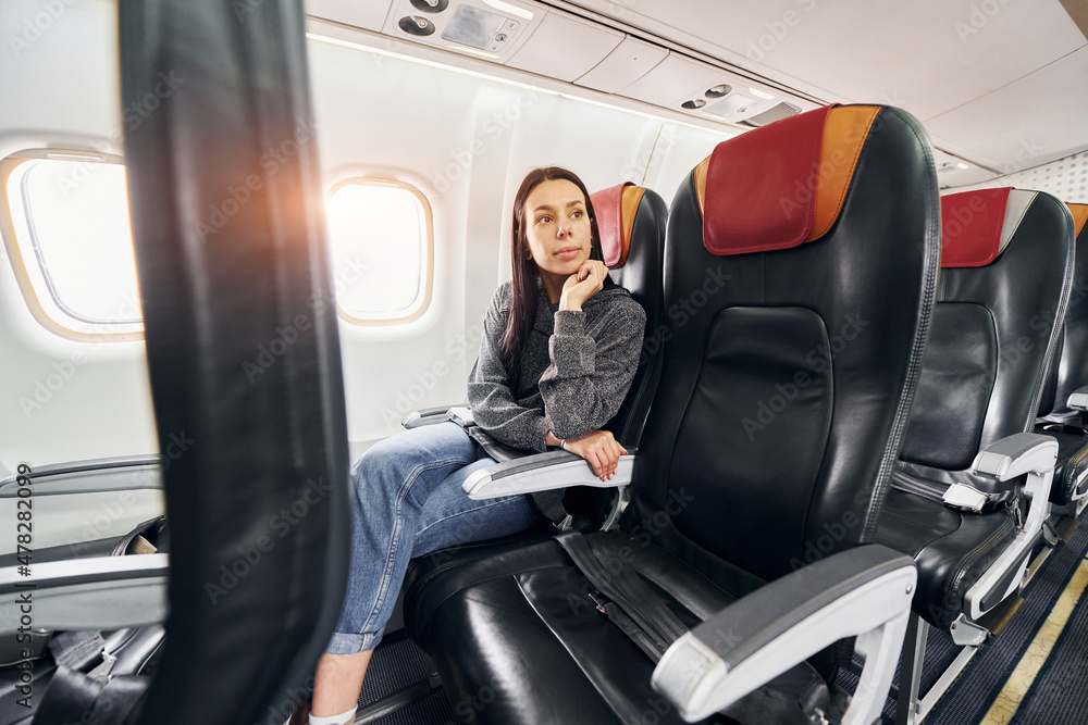 Young woman in casual clothes sits on the passenger seat in the plane Young woman in casual clothes sits on the passenger seat in the plane