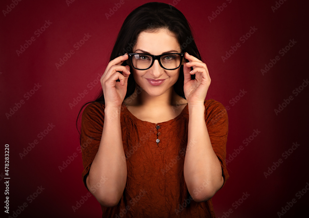 Beautiful thinking smiling happy woman looking happy in eye glasses and holding spectacles in casual orange t-shirt on red background with empty copy space. Closeup Beautiful thinking smiling happy woman looking happy in eye glasses and holding spectacles in casual orange t-shirt on red background with empty copy space. Closeup